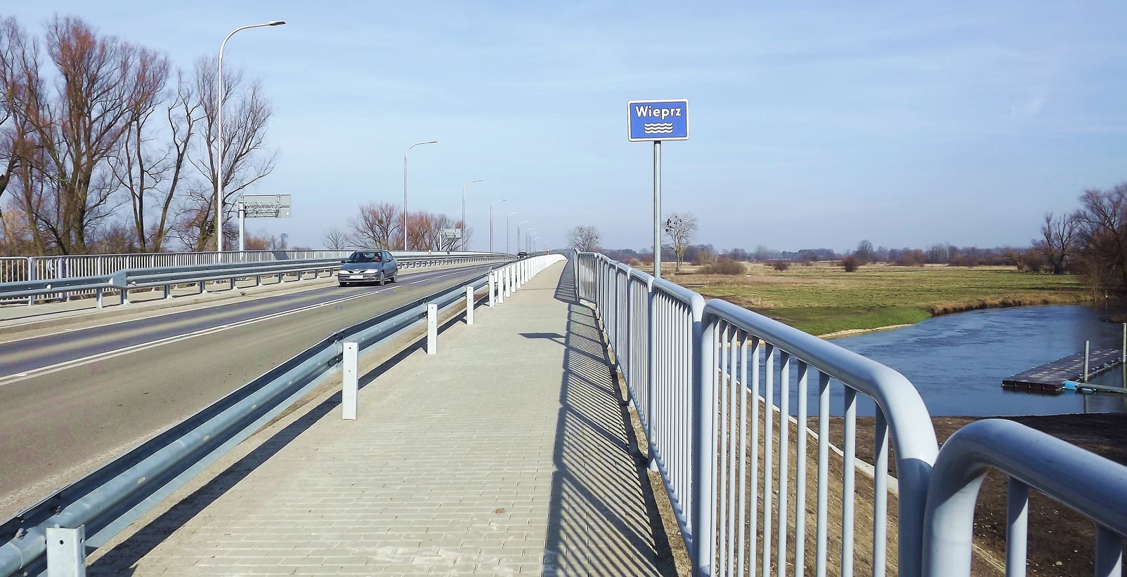Zdjęcie przedstawia chodnik wraz z barierkami ochronnymi na moście w Trawnikach