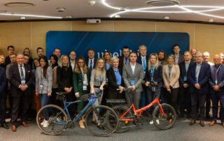 Zdjęcie przedstawia wszystkich uczestników spotkania zespołu do spraw mobilności rowerowej. Z przodu, przed uczestnikami stoją dwa rowery. Jeden pomarańczowy drugi niebieski.