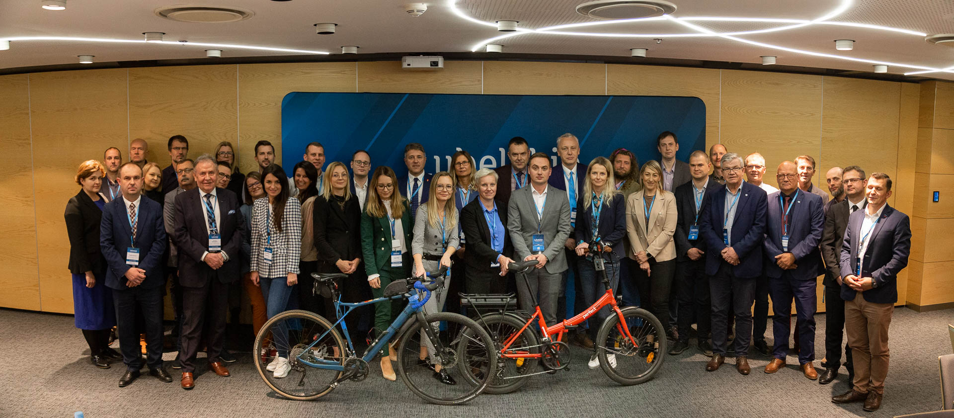 Zdjęcie przedstawia wszystkich uczestników spotkania zespołu do spraw mobilności rowerowej. Z przodu, przed uczestnikami stoją dwa rowery. Jeden pomarańczowy drugi niebieski.
