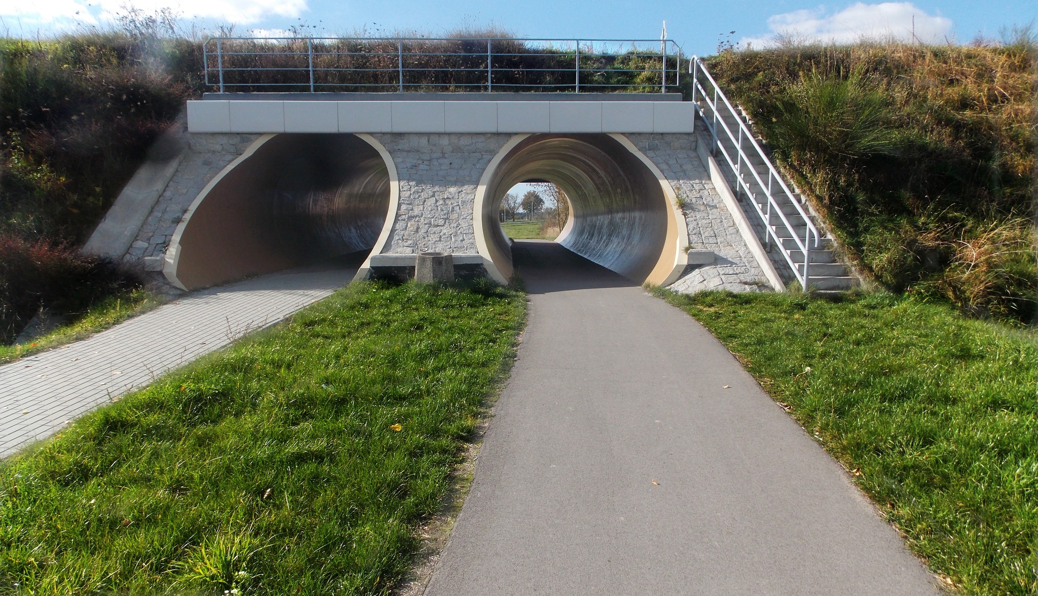 Zdjęcie przedstawia ścieżkę rowerową i ciąg pieszo-rowerowy zbudowany tuż obok drogi wojewódzkiej numer 815 z Parczewa do Lubartowa. Przebiegają one pod torami kolejowymi i znajdują się w tunelu.