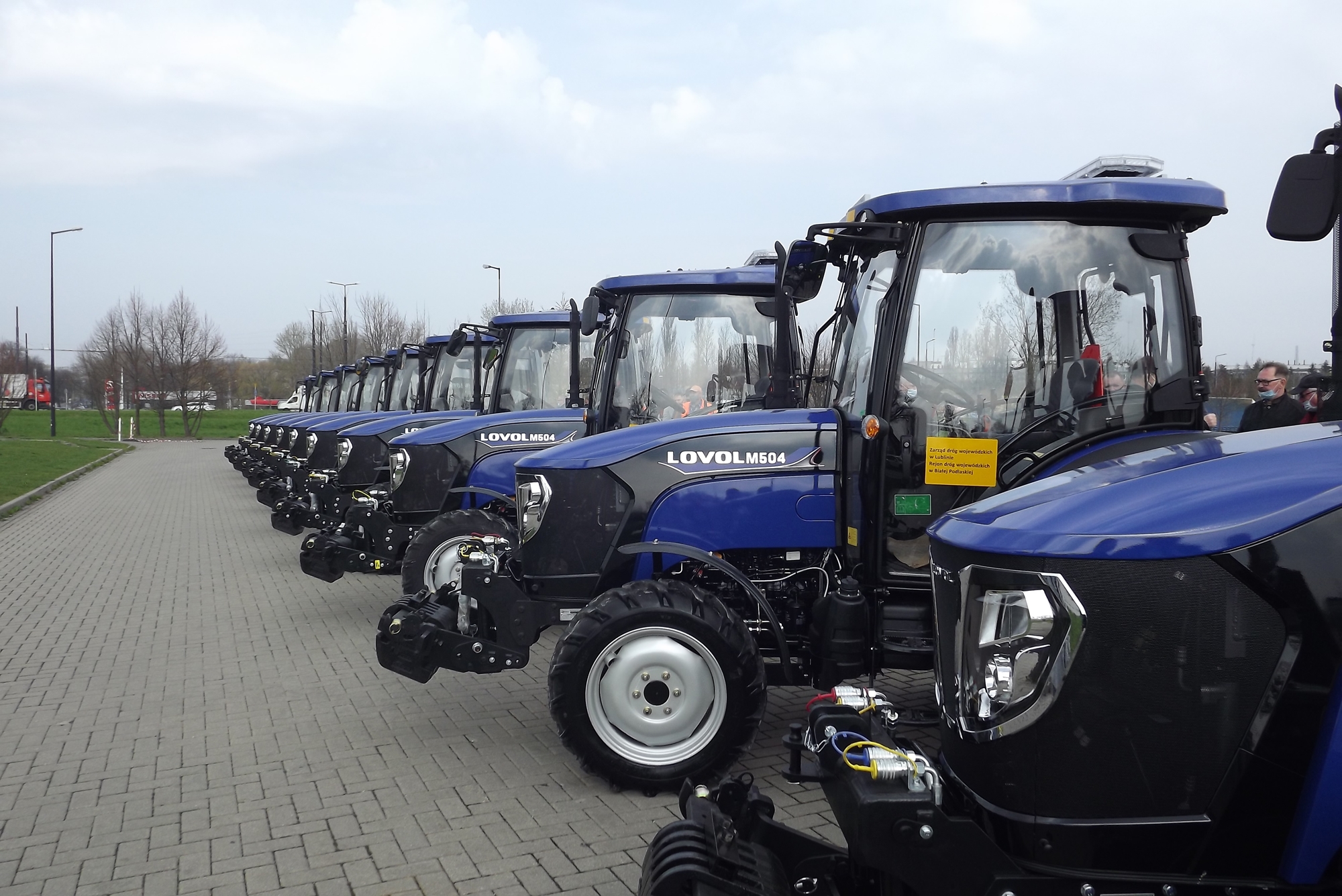 Na zdjęciu widzimy ustawione w szeregu małe ciągniki marki Lovol koloru niebieskiego, które będą służyły w Rejonach Dróg Wojewódzkich