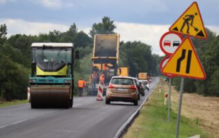 Zdjęcie przedstawia pracujący sprzęt do budowy dróg - walce drogowe, rozścielacz do masy bitumicznej, samochody ciężarowe z masą bitumiczną, na remontowanym odcinku drogi wojewódzkiej numer 844