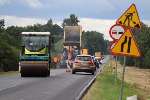 Zdjęcie przedstawia pracujący sprzęt do budowy dróg - walce drogowe, rozścielacz do masy bitumicznej, samochody ciężarowe z masą bitumiczną, na remontowanym odcinku drogi wojewódzkiej numer 844