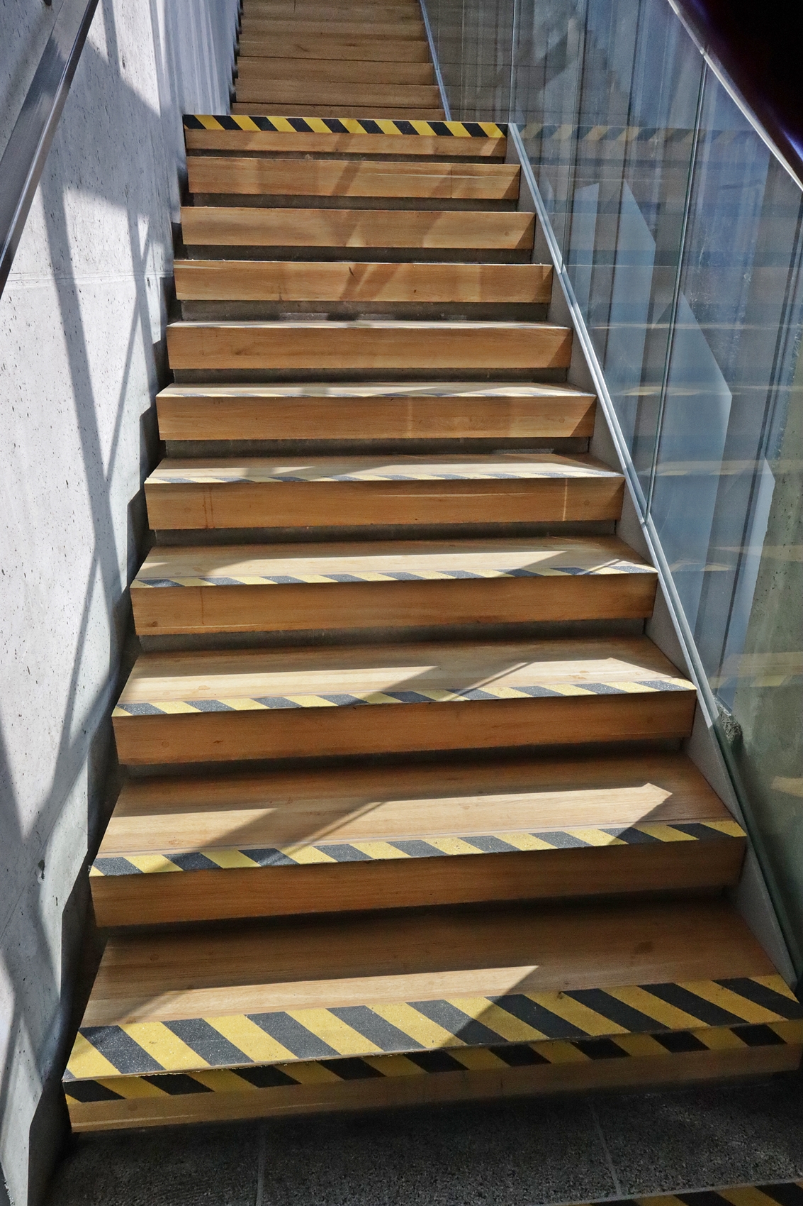 Na zdjęciu widzimy drewniane schody wykonane z jasnego drewna, które prowadzą na piętro w Zarządzie Dróg Wojewódzkich w Lublinie. Jest ich łącznie 16 i przedzielone są miejscem spoczynkowym po przejściu 8 schodków. Po lewej stronie znajduje się poręcz umiejscowiona na wysokości 90 cm i 115 centymetrów.