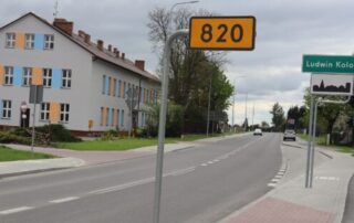 Zdjęcie przedstawia drogę wojewódzką numer 820 która biegnie od Łęcznej do miejscowości Sosnowica. Zdjęcie wykonane w miejscowości Ludwin. Po prawej stronie widzimy tabliczkę informacyjną, prostokątną, koloru żółtego, z numerem 820 w kolorze czarnym. W tle, po tej samej stronie widzimy zieloną tablicę informacyjną z nazwą miejscowości - Ludwin Kolonia. Po lewej stronie zdjęcia, w jego tle, widzimy budynek szkoły podstawowej w Ludwinie Kolonii.